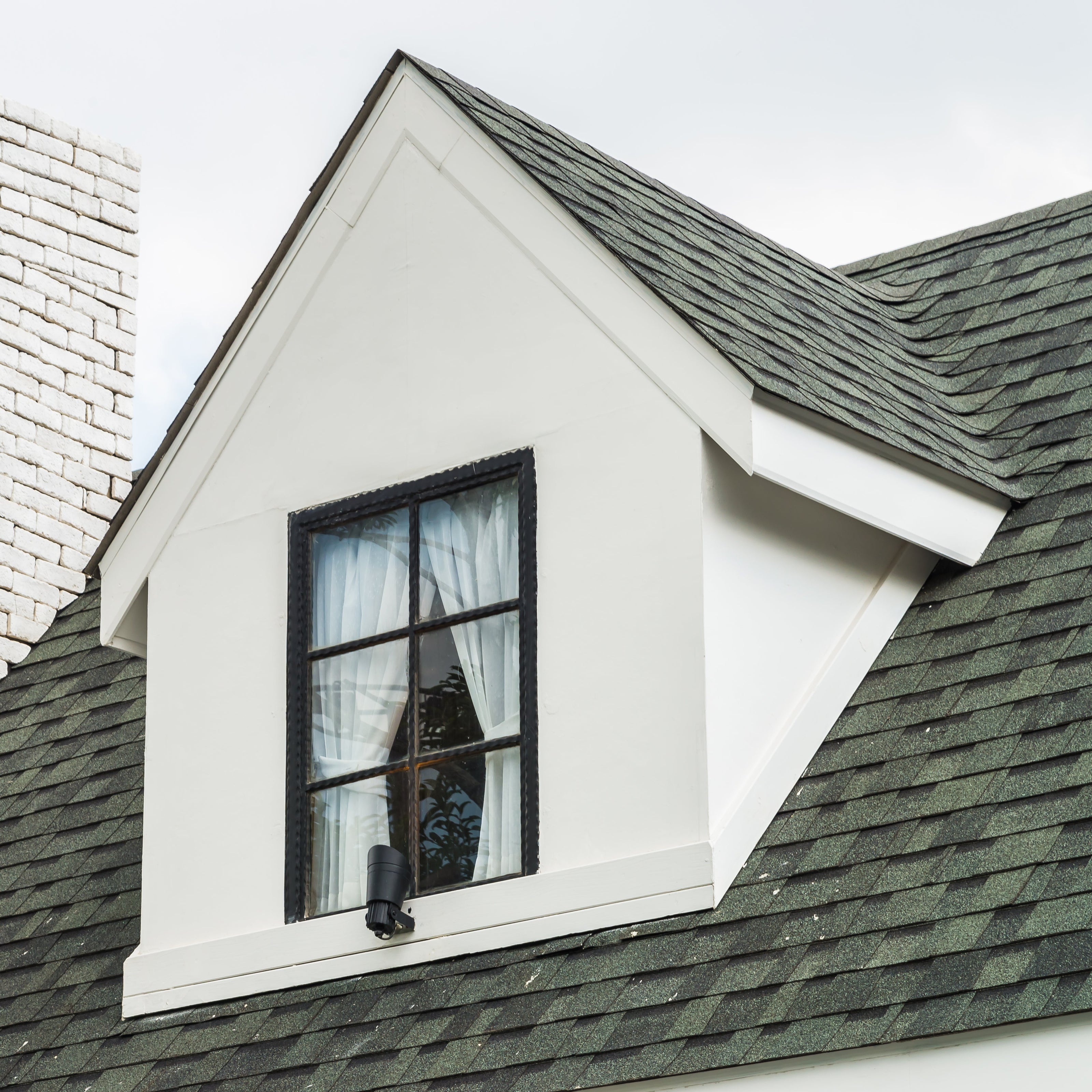 Attic window with white trim on a roof with a chimney